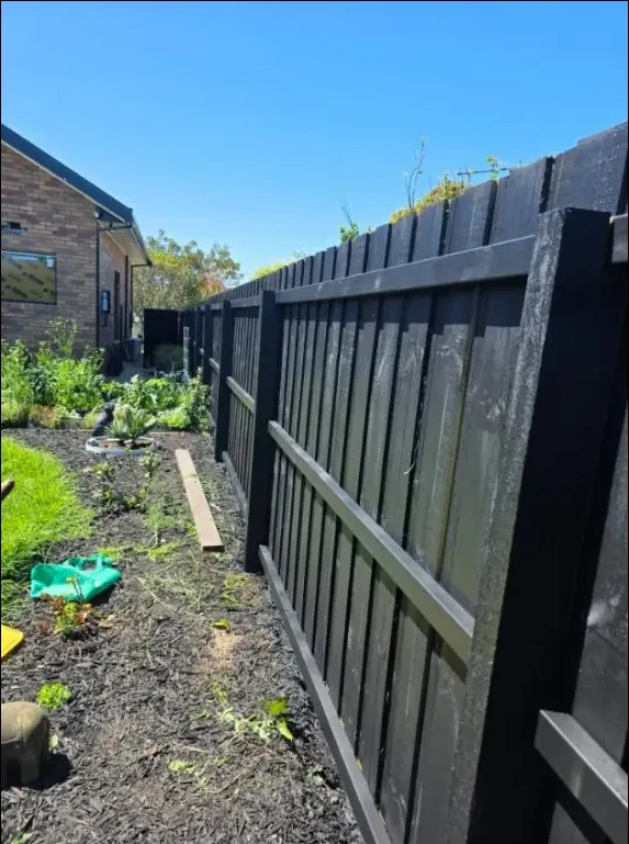 Charcoal timber paling fence painted along a backyard garden beside a brick home in Grovedale