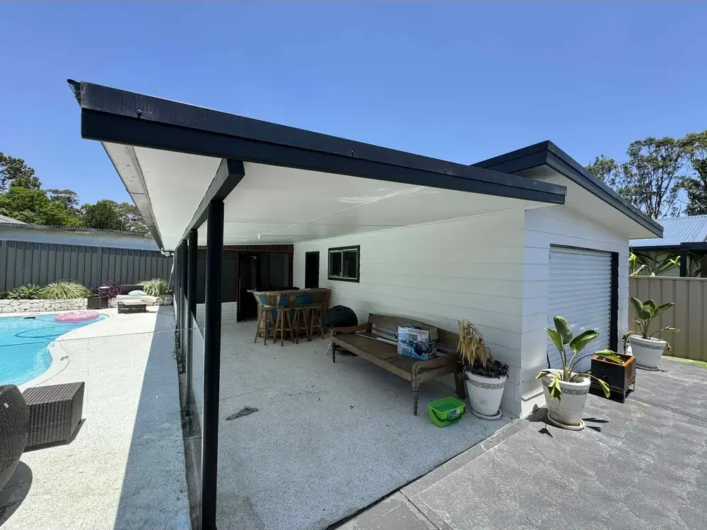 Covered outdoor entertaining area beside a swimming pool in Highton, with white cladding and black fascia and posts